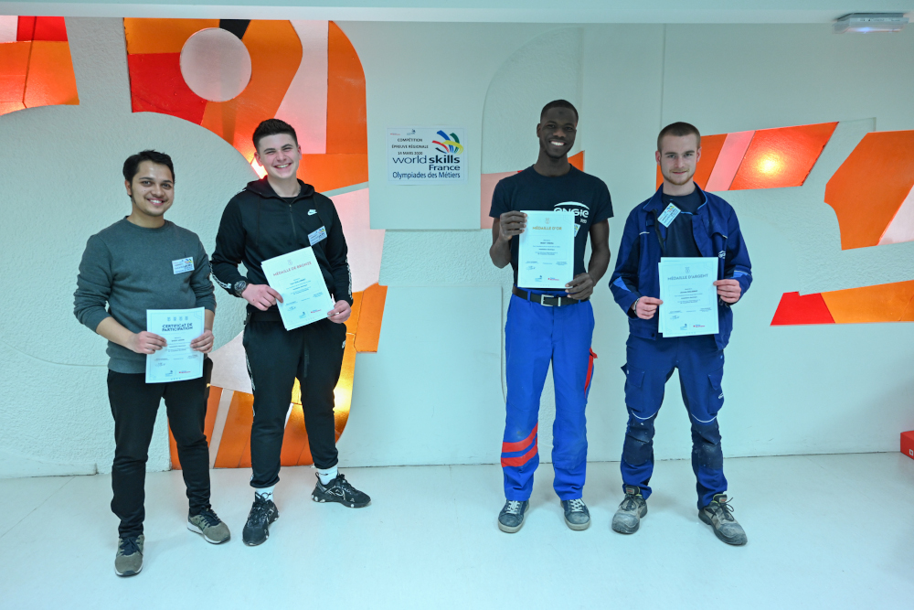 Les quatre compétiteurs de l'épreuve régionale des Worlds Skills 2020 métier électricien posent avec leurs diplômes devant le vitrail du CFA Delépine.