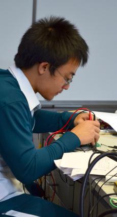 Un apprenti en CAP Electricien est penché sur sa table de travail, entre des instruments de mesure et des feuilles de note.
